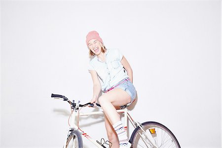 Studio shot of young woman laughing whilst sitting on bicycle Stock Photo - Premium Royalty-Free, Code: 649-08117842