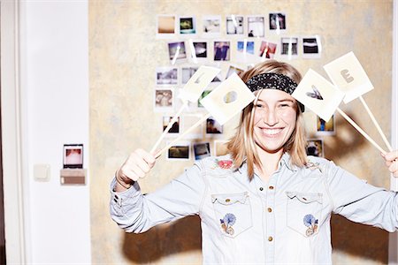 Young woman in front of photo wall holding up love sign Stock Photo - Premium Royalty-Free, Code: 649-08117858