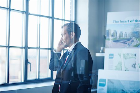 Business man chatting on smartphone whilst looking out of office window Stock Photo - Premium Royalty-Free, Code: 649-08117870