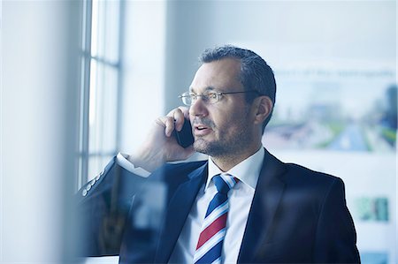 Business man chatting on smartphone whilst looking out of window Stock Photo - Premium Royalty-Free, Code: 649-08117871
