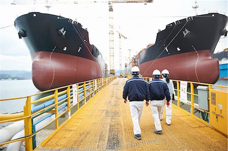 simsearch:649-08118274,k - Three workers walking towards ships at shipping port, rear view, GoSeong-gun, South Korea Stock Photo - Premium Royalty-Free, Code: 649-08118279