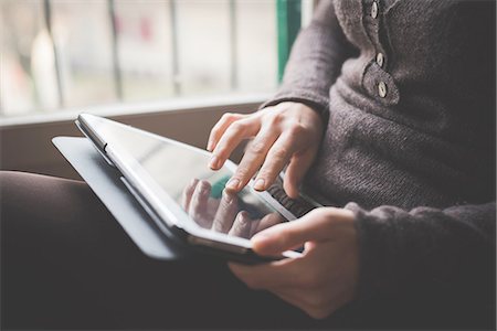 screen - Young woman sitting by window, using digital tablet, focus on hands Stock Photo - Premium Royalty-Free, Code: 649-08118590