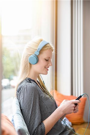 simsearch:649-08118646,k - Young woman, wearing headphones, sitting in cafe, holding smartphone Stock Photo - Premium Royalty-Free, Code: 649-08118645