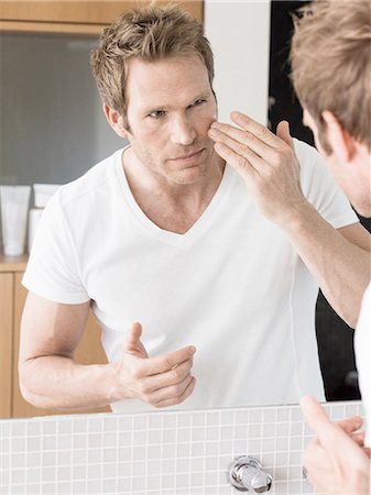 simsearch:649-08179955,k - Mid adult man looking in bathroom mirror applying face cream Fotografie stock - Premium Royalty-Free, Codice: 649-08118748