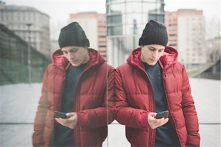 simsearch:649-08118826,k - Mirror image of young man leaning against office building reading smartphone texts Foto de stock - Sin royalties Premium, Código: 649-08118868