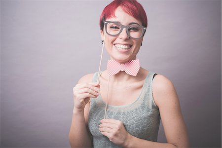 Studio portrait of confused young woman holding up spectacles in front of face Stock Photo - Premium Royalty-Free, Code: 649-08125676