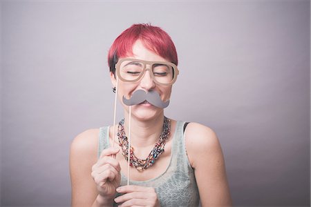disguise - Studio portrait of young woman holding up mustache and spectacles in front of face Stock Photo - Premium Royalty-Free, Code: 649-08125673