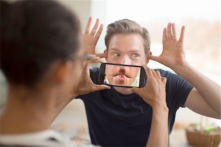 Woman holding smartphone in front of man's mouth Stock Photo - Premium Royalty-Free, Code: 649-08144574