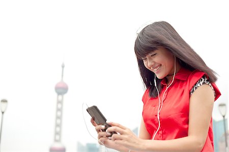 simsearch:649-08145347,k - Young woman wearing earphones, looking at smartphone, Shanghai, China Stock Photo - Premium Royalty-Free, Code: 649-08145359