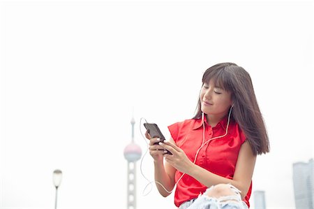 simsearch:649-08145347,k - Young woman wearing earphones, looking at smartphone, Shanghai, China Stock Photo - Premium Royalty-Free, Code: 649-08145360