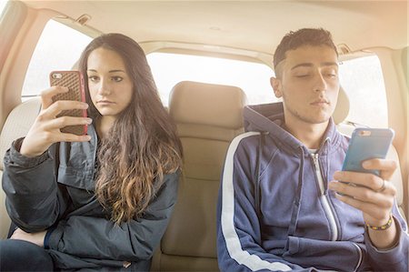people sharing car - Teenage girl and young man reading separate smartphone texts in car back seat Stock Photo - Premium Royalty-Free, Code: 649-08145563
