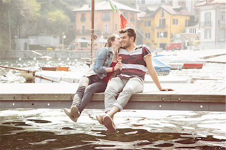 Couple sitting on pier whispering and eating ice cream cone at lake Mergozzo, Verbania, Piemonte, Italy Foto de stock - Royalty Free Premium, Número: 649-08145630