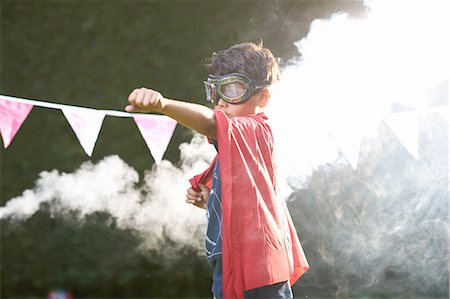 Boy wearing goggles and cape in superhero stance in front of smoke cloud Photographie de stock - Premium Libres de Droits, Code: 649-08179760