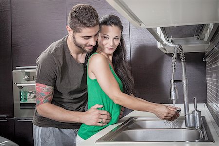 simsearch:649-08179955,k - Young woman washing up whilst being embraced by boyfriend Fotografie stock - Premium Royalty-Free, Codice: 649-08179945