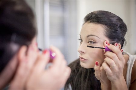 simsearch:649-08179955,k - Over the shoulder mirror image of young woman applying mascara Fotografie stock - Premium Royalty-Free, Codice: 649-08179942