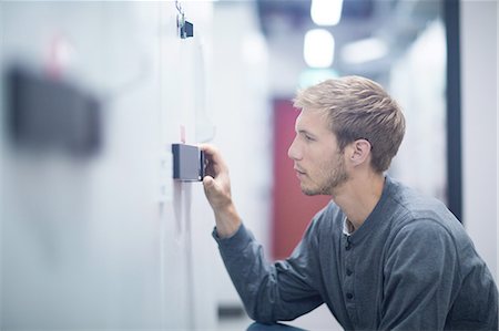 Male technician crouching to turn switch in technical room Stock Photo - Premium Royalty-Free, Code: 649-08180031