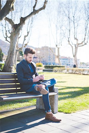 Young man sitting on park bench reading smartphone texts Stock Photo - Premium Royalty-Free, Code: 649-08180055
