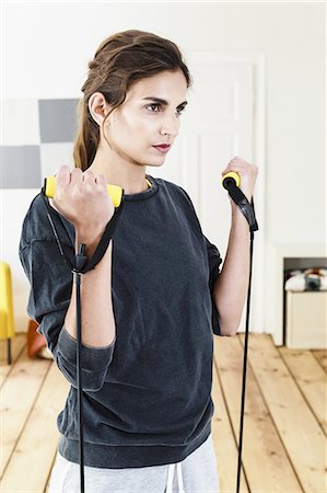 Young woman exercising with resistance bands in living room Stock Photo - Premium Royalty-Free, Code: 649-08180457