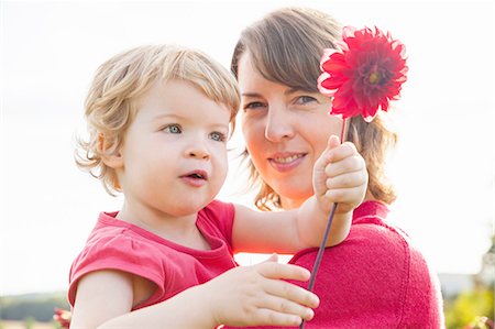 simsearch:633-02417965,k - Portrait of mid adult mother and toddler daughter holding red flower in field Fotografie stock - Premium Royalty-Free, Codice: 649-08180677