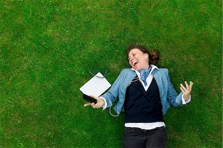 Overhead view of mature woman lying on grass laughing whilst listening to smartphone music Stock Photo - Premium Royalty-Free, Code: 649-08237633