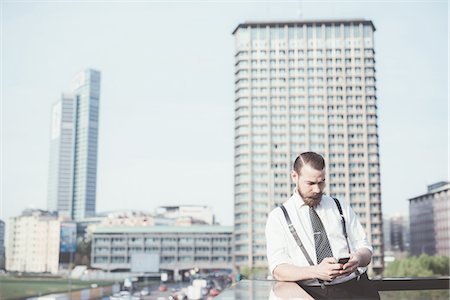 Stylish businessman reading smartphone text update on office balcony Stock Photo - Premium Royalty-Free, Code: 649-08237682