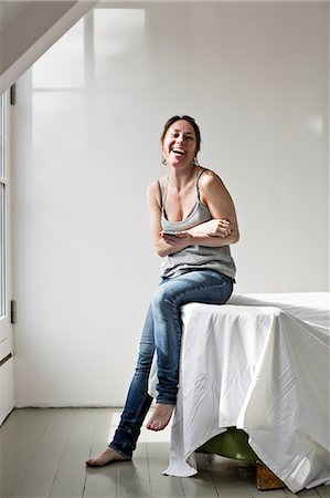 escaso - Mature woman leaning on sofa in part furnished home, using mobile phone, laughing Foto de stock - Sin royalties Premium, Código: 649-08237713