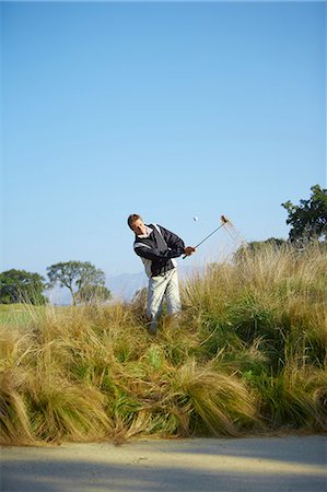 Golfer taking golf swing in tall grass, golf ball in mid air Stock Photo - Premium Royalty-Free, Code: 649-08238394