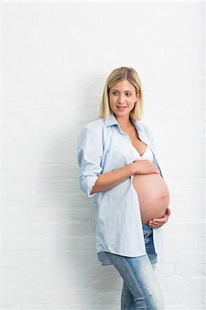 pregnant smiling hold stomach - Full term pregnancy young woman leaning against wall holding stomach Stock Photo - Premium Royalty-Free, Code: 649-08238460