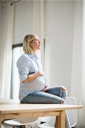 simsearch:649-08238461,k - Full term pregnancy young woman sitting on table holding stomach Foto de stock - Sin royalties Premium, Código: 649-08238462