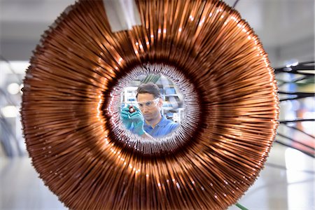 Worker inspecting electromagnetic coil seen through large coil in electromagnetics factory Stock Photo - Premium Royalty-Free, Code: 649-08238647