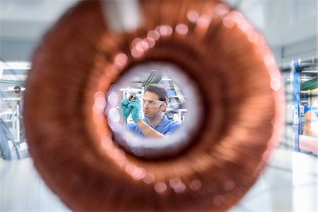protective glove - Worker inspecting electromagnetic coil seen through large coil in electromagnetics factory Stock Photo - Premium Royalty-Free, Code: 649-08238648