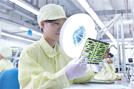 Female worker using magnifying glass at quality check station for a factory producing flexible electronic circuit boards. Plant is located in the south of China, in Zhuhai, Guangdong province Stock Photo - Premium Royalty-Free, Code: 649-08238659