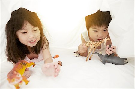 simsearch:640-06963758,k - Young Chinese boy and girl in bed playing with their toys under the bedsheets Foto de stock - Royalty Free Premium, Número: 649-08239014