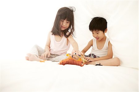 simsearch:640-06963758,k - Young Chinese boy and girl in bed playing with their toys under the bedsheets Foto de stock - Royalty Free Premium, Número: 649-08239013