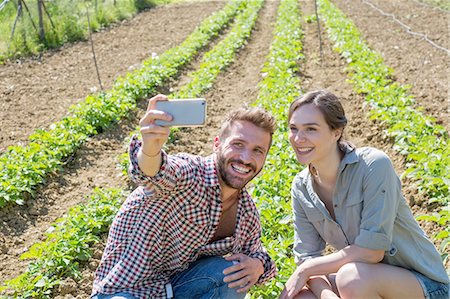 simsearch:649-08239053,k - Young couple crouched in vegetable garden using smartphone to take selfie Foto de stock - Sin royalties Premium, Código: 649-08239060