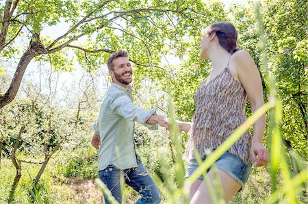 simsearch:649-08239072,k - Young couple holding hands in forest fooling around smiling Foto de stock - Sin royalties Premium, Código: 649-08239084