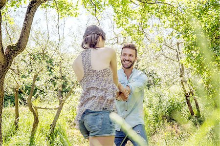 simsearch:649-08239072,k - Young couple holding hands in forest fooling around smiling Foto de stock - Sin royalties Premium, Código: 649-08239083