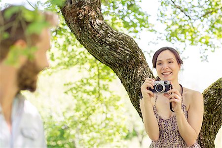Young woman underneath tree taking photograph of young man Stock Photo - Premium Royalty-Free, Code: 649-08239091