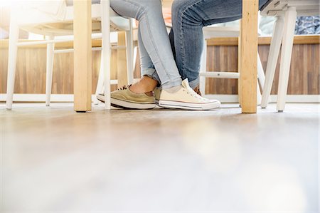 Surface level view of couples entwined legs sitting at table face to face Stock Photo - Premium Royalty-Free, Code: 649-08232411