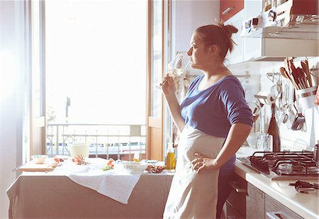 female with apron in kitchen - Mid adult woman taking a cooking break and drinking white wine in kitchen Stock Photo - Premium Royalty-Free, Code: 649-08232583