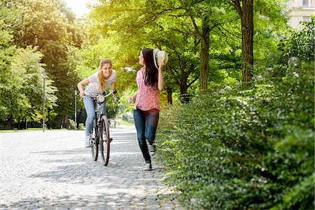 simsearch:649-08306424,k - Front view of young smiling woman on bicycle chasing young woman holding panama hat Photographie de stock - Premium Libres de Droits, Code: 649-08232661