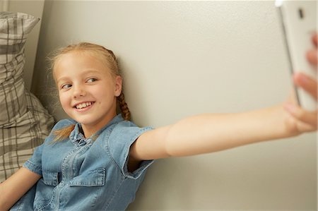 Girl sitting leaning against wall using smartphone to take selfie smiling Stock Photo - Premium Royalty-Free, Code: 649-08306404