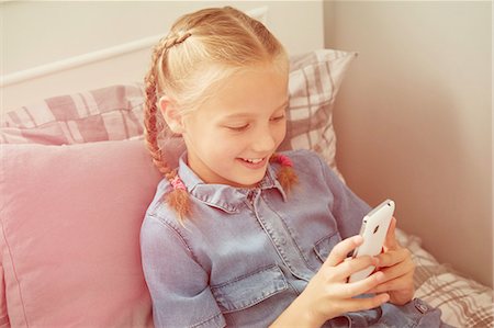 High angle view of girl sitting on bed looking down at smartphone smiling Fotografie stock - Premium Royalty-Free, Codice: 649-08306406