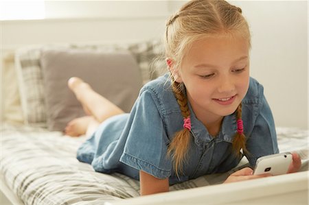 Girl lying on bed looking down at smartphone smilinhg Photographie de stock - Premium Libres de Droits, Code: 649-08306401