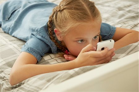 High angle view of girl lying on bed looking at smartphone Fotografie stock - Premium Royalty-Free, Codice: 649-08306402