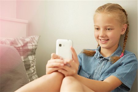 Girl sitting leaning against wall looking at smartphone smiling Fotografie stock - Premium Royalty-Free, Codice: 649-08306403