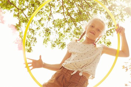 pigtails girl - Low angle view of girl looking through hula hoop at camera smiling Stock Photo - Premium Royalty-Free, Code: 649-08306427