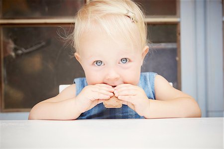 simsearch:649-08306549,k - Portrait of cute blonde baby girl looking at camera eating chocolate biscuit Foto de stock - Sin royalties Premium, Código: 649-08306435