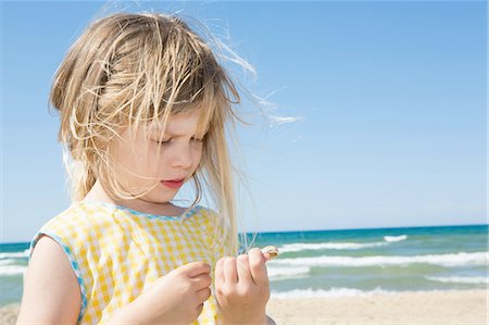 simsearch:649-08306543,k - Girl with blond flyaway hair looking at seashell on beach Stock Photo - Premium Royalty-Free, Code: 649-08306544