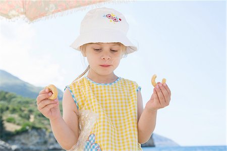 simsearch:649-08306545,k - Girl wearing sunhat eating doughnut on beach Stock Photo - Premium Royalty-Free, Code: 649-08306548